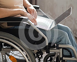 Caucasian woman in a wheelchair typing with a laptop from home. Remote work for people with disabilities.