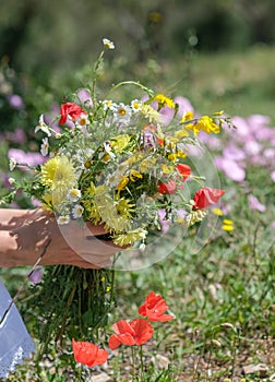 caucasian woman in white dress holding wild flowers bouquet in hands