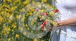 caucasian woman in white dress holds wild flowers bouquet on floral background