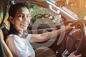 Caucasian woman in a white shirt, driving, and smiling looking camera