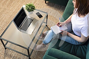 Caucasian woman working at home with laptop and notebook. Write a note on the book with a pen like old fashioned but use internet