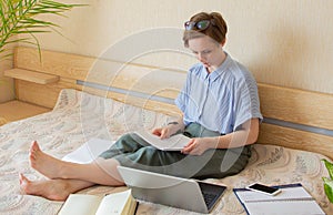 Caucasian woman working with laptop at home on the bed at home. Young female working cozy office workplace, remote work