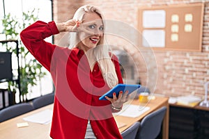 Caucasian woman working at the office with tablet doing peace symbol with fingers over face, smiling cheerful showing victory