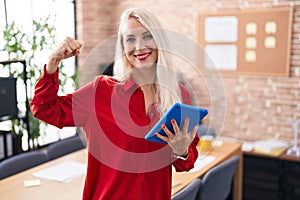 Caucasian woman working at the office with tablet strong person showing arm muscle, confident and proud of power