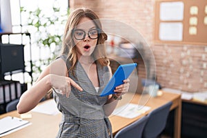 Caucasian woman working at the office wearing glasses pointing down with fingers showing advertisement, surprised face and open