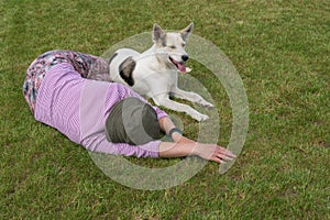 Caucasian woman and  young white mixed breed dog lying next to each other on a cut lawn