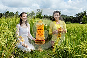 Caucasian women dressed in traditional Balinese costumes preparing offerings for Hindu religious ceremony. Culture and religion.
