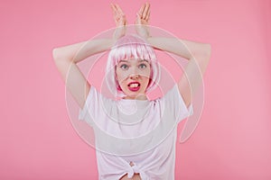 Caucasian wonderful girl in pink peruke making funny faces on pastel background. Studio shot of win