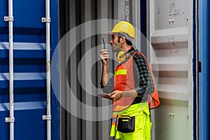 Caucasian worker in safety vest reflective with Safety helmet talking on radio and looking into empty container box