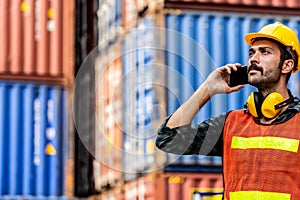 Caucasian worker in safety vest reflective with Safety helmet talking to the phone in container yard