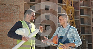 Caucasian workers in uniform talking near building construction
