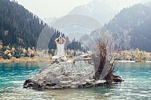 Caucasian yoga man in outdoor meditation sitting on lonely rock island of mountain lake