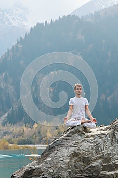 Caucasian yoga man in outdoor meditation sitting on lonely rock island of mountain lake