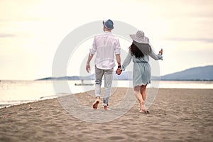 Caucasian young adult couple in love walking barefoot on sandy beach, holding hands