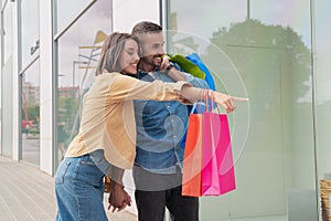 Caucasian young adult couple pointing finger at sales in city shopping center window.