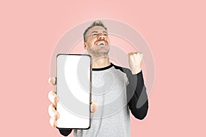 Caucasian young adult man smiling and celebrating while holding smart phone with white screen for copy space advertisement. Close