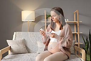 Caucasian young adult pregnant woman using mobile phone searching information and reading medicine label and prescription