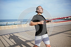 Caucasian young athletic man exercising with resistance fitness band, bodyweight workout sports training on a sunny day