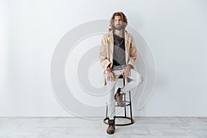 Caucasian young bearded man sitting isolated over grey wall