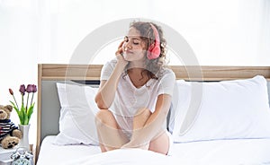 Caucasian young and beautiful happy woman with headphone sitting on the  comfortable  double bed in the modern bedroom
