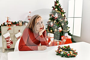 Caucasian young blonde woman sitting on the table by christmas tree thinking looking tired and bored with depression problems with