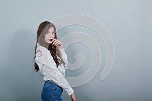 Caucasian young brunette lady, staying sideways, holding finger on mouth, posing