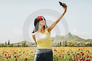 Caucasian young carefree woman hold poppy flower in ears stand in poppy flower field take selfie enjoy springtime. Concept freedom