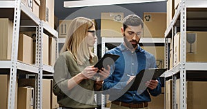 Caucasian young couple of male and female postal workers standing in mail store with carton boxes, talking and