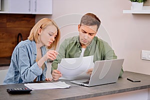 Caucasian young couple reading and analyzing bills sitting at table