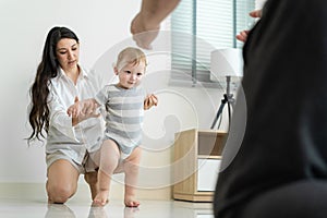 Caucasian young cute baby boy child learn to walk with parent in house. Happy family mother support little toddler son taking