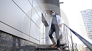 Caucasian young doctor man sits down on the stairs near the clinic building, tired and unhappy rubbing his nose and eyes