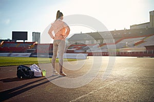 Caucasian young female standing at the athletic track with hands on hips, preparing for training, visualizing goal