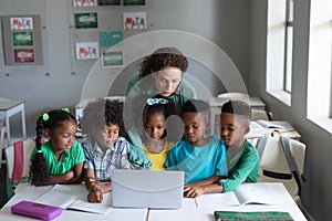 Caucasian young female teacher teaching laptop to african american elementary students in class