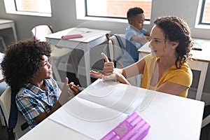 Caucasian young female teacher teaching sign language to african american elementary boy in class