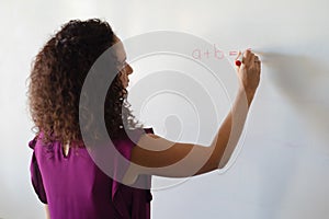 Caucasian young female teacher writing formula on whiteboard during math class in school