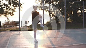 Caucasian young fit woman in hoodie and shorts warming up in morning on basketball court. Stretching her legs before