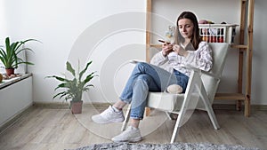 Caucasian young girl knits sitting in a chair at home, the concept of knitting and needlework, women's hobbies and