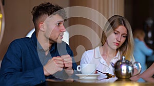 Caucasian young handsome serious man speaking with pretty woman while sitting in restaurant. Boyfriend and girlfriend