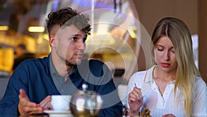 Caucasian young handsome serious man speaking with pretty woman while sitting in restaurant. Boyfriend and girlfriend