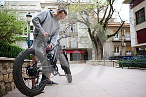 Caucasian young man adjusts the height of new battery powered bike, electric bicycle before taking it out for first ride