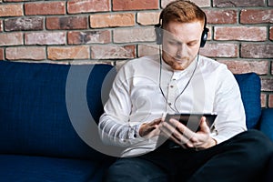 Caucasian young man in headphones watching movie on tablet computer w