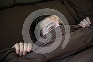 Caucasian young man hiding in bed under the blanket at home.
