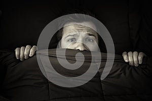 Caucasian young man hiding in bed under the blanket at home.