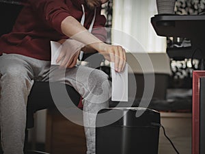 Caucasian young man inserts a sheet of paper for destruction in a black shredder