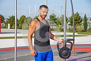Caucasian young man lifts weights doing exercises for biceps on an equipped sports ground in a city park. Workout with heavy