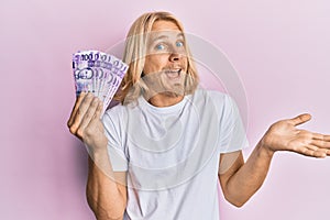 Caucasian young man with long hair holding 100 philippine peso banknotes celebrating achievement with happy smile and winner