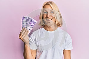 Caucasian young man with long hair holding 100 philippine peso banknotes looking positive and happy standing and smiling with a