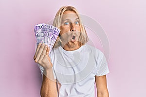 Caucasian young man with long hair holding 100 philippine peso banknotes scared and amazed with open mouth for surprise, disbelief