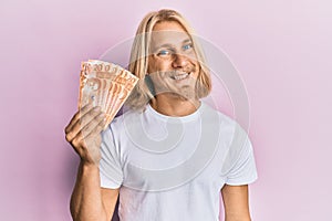 Caucasian young man with long hair holding 20 philippine peso banknotes looking positive and happy standing and smiling with a