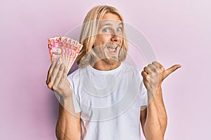 Caucasian young man with long hair holding 50 philippine peso banknotes pointing thumb up to the side smiling happy with open